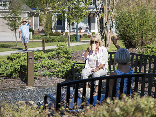 Neighbors waving as they drink coffee in the park.>